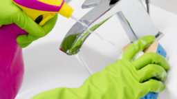 Hands in latex gloves clean a faucet with cleaner and sponge