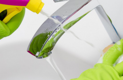 Hands in latex gloves clean a faucet with cleaner and sponge