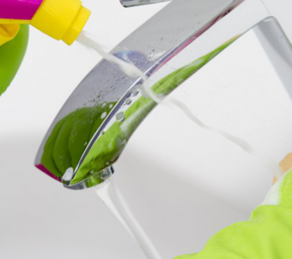 Hands in latex gloves clean a faucet with cleaner and sponge