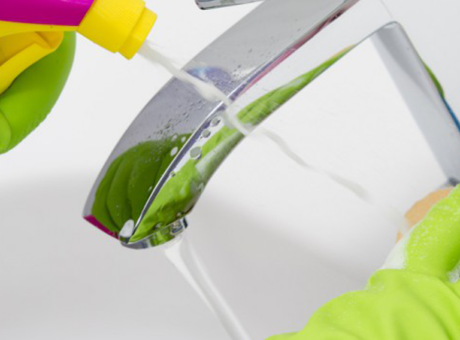 Hands in latex gloves clean a faucet with cleaner and sponge