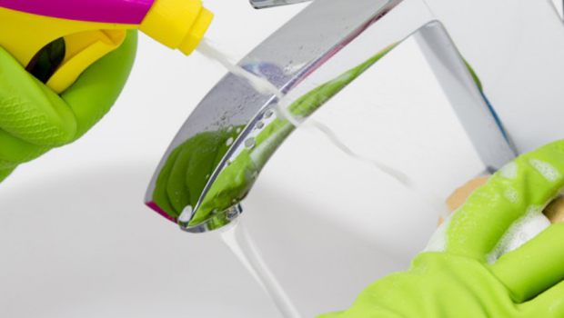 Hands in latex gloves clean a faucet with cleaner and sponge