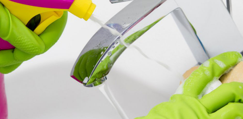 Hands in latex gloves clean a faucet with cleaner and sponge